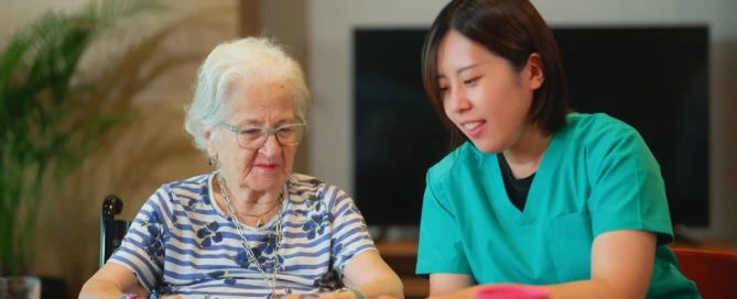 Senior woman folding towels with caregiver in memory care community to give them a familiar routines everyday