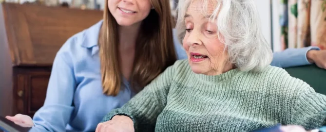 Assisted Living to Memory Care: caregiver and senior woman look through photo album at home