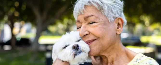 Pet-Friendly Assisted Care: senior woman cuddles a small dog outdoors in a park